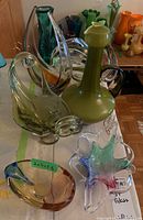 Overview of multiple colorful art glass vases, bowls, and candy dishes on a table, showcasing shapes and colors.