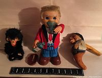 Bartender doll, carved folk art nutcracker figure, and small furry monkey toy shown with measuring scale for size reference