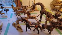 Photo showing the collection of brass animal figurines including giraffe, horses, dog and others on a light surface.