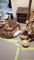 Wide view photo showing multiple brass trays, trivets, and incense burners arranged on table