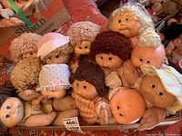 Group of 10 needle-molded Cabbage Patch Dolls piled together in a box, showing various hair styles, clothing, and facial expressions, displaying age-related stains and wear.