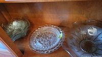 Candy dish, bowls and plates displayed on a shelf showing clear pressed glass with floral and iris pattern