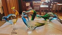 Photo showing four glass animal figurines in blue, green, and yellow accents on a white cloth.