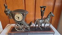 Wide view of the horse and buggy mantel clock on its base showing the driver, horse, buggy wheels, and clock face.