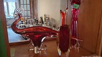 View showing glass bird figurine and taller red Murano vase with long neck and flared opening.