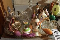 Full set of various vintage perfume atomizers and bottles on a gold-tone decorative tray with floral designs and bulbs in pink, orange, and purple.