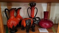 Photo showing entire lot including Bernard Moore red vase, black elephant figurine with orange glaze, and three orange-glazed pitchers.