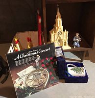 Wide view showing the Avon Christmas album, Spode mug in display box, electric red candles, church music box, and figurine on a wooden shelf.