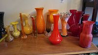 Wide arrangement of 12 glass vases in various colors and shapes on wooden table.