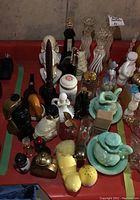 Photo showing the assortment of Avon collectible bottles including bust style bottles, shaped glass bottles in black and amber, and small decorative items on a red surface.