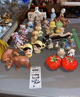 Overview of multiple salt and pepper shakers arranged on table showing variety of animal and character designs including cats, dogs, birds, children, bears, tomatoes and more.