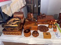 Full lot view showing multiple wood carved boxes, two wooden elephant figurines, and three painted nesting dolls on a white cloth.