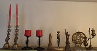 Full view of brass candlesticks with etched glass, black metal candle holders with red candles, Egyptian statues, brass picture holder and trivet.