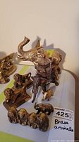 Lot of various brass animal figurines including elephants, lions, and a monkey figure arranged on a flat surface with handwritten lot label.