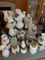 Overview of assorted porcelain and milk glass oil lamps showing floral decals, varying sizes and shapes.