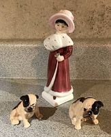 Front view of three figurines: Sophie in maroon dress and two seated bulldogs, one larger adult and one small puppy.