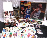 Wide shot of box of NBA trading cards, Larry Bird 8x10 photo, Funko Pop Gold Ja Morant figure, and scattered trading cards on table