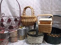Photo showing 5 baskets in front and 15 rolls of ribbon stacked behind them. The baskets include 2 metal baskets with leaf designs and 3 woven baskets of natural materials.