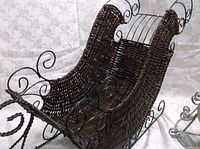 Close-up of the dark brown wicker holiday sleigh with metal framing and scroll detail.