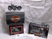 Three Harley Davidson 1:18 scale motorcycles and ornament in original packaging, including 1948 FL Panhead with certificate, police series model, and teal ornament.