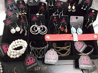 Photo showing multiple pairs of earrings on Paparazzi cards, several bracelets including pearl cluster and silver bangles, laid out on a black surface