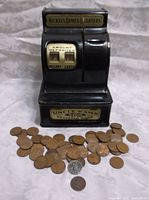 Full view of Uncle Sam's 3 Coin Register Bank with a spread of vintage pennies including the Indian Head and wheat pennies visible in front