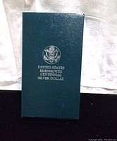 Closed dark green display box for the United States Eisenhower Centennial Silver Dollar with embossed seal and labeling.