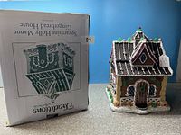 Front view of gingerbread house figurine next to its original box showing detailed front façade and roof.