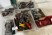 Overview of assorted door locks, hardware, nails in a glass jar, and assorted hand tools in plastic bins, showing some rust and wear.