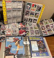 Wide shot showing binder with multiple sports cards in plastic sleeves, and magazines on the table.