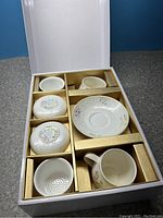 Open box showing Chinaware set items including teapot, cups, saucer, and infuser.