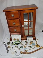 Jewelry box with drawers and glass door alongside various pieces of vintage costume jewelry spread out in front.