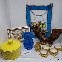 Full lot view showing yellow covered jar, blue glass owl, brown double spout vase, snuff bottle, candles, floral plaque and stained glass hanging