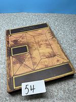 Front cover of the heritage book with an ornate, aged leather design and gold embossed rectangles.