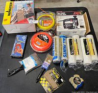 Overview of entire lot showing boxed Wagner Power Painter Kit, Skil scroll saw box, paint rollers, paint brushes, tape measure, and trimmer lines.
