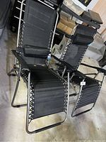 Pair of zero gravity lounge chairs in black with silver metal frames, showing padded headrests and elastic cord lacing connecting fabric to frames.