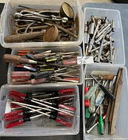 Four plastic bins containing various hand tools including screwdrivers, hammers, and socket wrenches. Tools show signs of rust and heavy use.