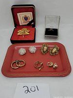 Photo showing all jewelry items including Trifari pin in red box, ring in clear box, hoop earrings, crystal clip earrings, and tray