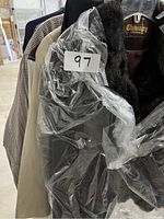 Several jackets hanging on rack, including a dark jacket with fur collar and a beige jacket, tagged with lot number 97.