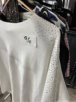 Close-up photo of a white long sleeve shirt with rhinestone embellishments on shoulder and sleeve with lot number 96.