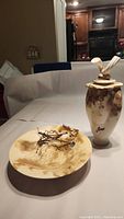 Photo showing the pit fired pottery bowl with natural branch and bead bull accent, and the pit fired pottery vase with lid and feathers on top