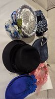 Six women's headwear items on couch including black wool hat, blue hats, a pink hat, and a blue fascinator.