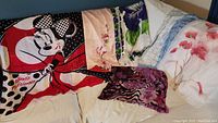 6 assorted scarves displayed on a couch, showing varied colors and patterns including Minnie Mouse and floral prints.