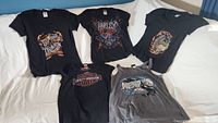 Six Harley Davidson ladies shirts laid out on a white surface, showing different graphics and styles, primarily black with one gray sleeveless shirt.