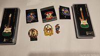 Eight Atlanta 1996 Olympic pins laid out, including two guitar shaped pins in plastic display cases, various sport-themed pins like baseball, equestrian, and gymnastics.