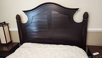 Front view of dark wood headboard attached to bed, showing arch top and pineapple detail on posts.