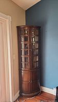 Frontal view of the full corner curio/bar cabinet showing curved glass-paned upper doors and curved wooden lower doors.
