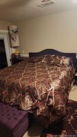 Overall view of bed with comforter and matching shams in brown, burgundy, and gold ornate pattern.