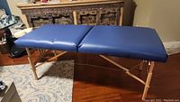Full view of blue vinyl padded massage table with wooden frame and folding legs.