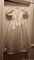 Full-length view of the ivory satin dress hanging, showing the silhouette including puffed sleeves and full skirt.